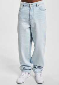 Vaqueros de mezclilla azul claro con un corte holgado, que cuentan con cierre de botón, diseño de cinco bolsillos y pierna recta. Combinados con zapatillas blancas.