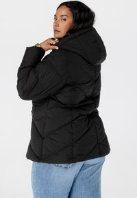 Zwarte pufferjack met een capuchon, voorzien van een geometrisch gewatteerd ontwerp en ritszakken. Draag het boven blauwe spijkerbroek.
