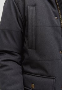 Ciemnoszara pikowana kurtka o teksturowanym wykończeniu, wyposażona w zamek błyskawiczny, kieszeń na guziki oraz przeszycie na rękawie.