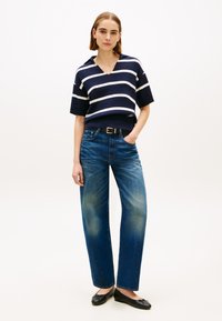 Πλεκτό τοπ σε ναυτικό μπλε και λευκές ρίγες με κοντά μανίκια και λαιμόκοψη σε σχήμα V, συνδυασμένο με τζιν παντελόνι με φαρδιά πόδια και μαύρες μπαλαρίνες. Υφή από denim και κομψή ζώνη.