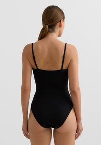 Črni enodelni kopalni kostim s tankimi nastavljivimi naramnicami, rebrasto teksturo in visokim izrezom na nogah. Gladek zaključek brez okraskov.