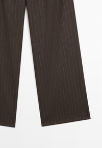 Pantalon de costume marron foncé avec fines rayures blanches verticales sur un fond blanc uni.