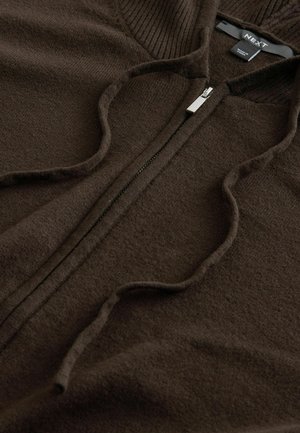 Rudas zip-up džemperis, pagamintas iš minkštos medžiagos. Yra raštuotas apykaklės tekstūra ir lygus kūnas su metaliniu užtrauktuku.