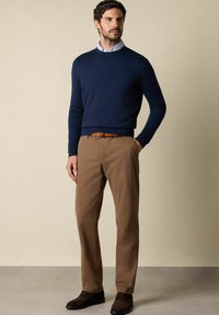 Maglione blu navy con scollatura rotonda, abbinato a pantaloni chinos color nocciola chiaro. Una cintura in pelle marrone e scarpe scure arricchiscono l'aspetto generale dell'outfit.
