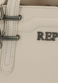 Borsa a tracolla beige chiaro con una texture in pelle liscia, dotata di accessori in argento, cuciture decorative e la parola "REPUBLIC" stampata.
