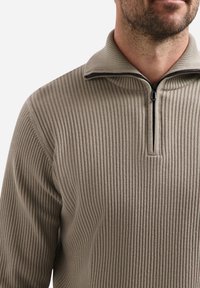 Beige geribde trui met een ritssluiting bij de kraag, voorzien van een textuurstof en een getailleerd ontwerp, gepresenteerd bij de hals en bovenlichaam.