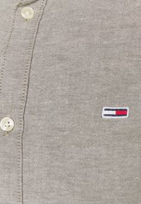 Gray button-up shirt featuring a textured fabric and a small embroidered logo with red, white, and blue accents near the chest.