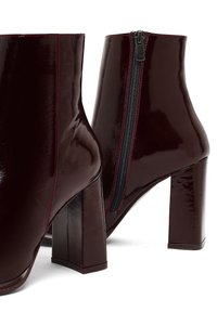 Stivaletti alla caviglia in pelle verniciata borgogna con tacco quadrato, zip laterale e dettagli in cucitura rossa a contrasto. Design elegante e moderno.