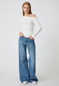 Witte off-shoulder top met lange mouwen, gecombineerd met hoge taille, losse blauwe jeans. Opmerkelijke details zijn het wijde pijpdesign en de soepele textuur.