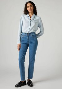 Camicia azzurra chiara con bottoni, jeans blu a vita alta e scarpe nere. I jeans hanno una vestibilità dritta e dettagli di cucitura minimi.