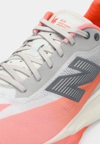 Chaussure de course orange et gris avec une tige en maille, rehaussée par des superpositions texturées et un logo réfléchissant. Présente un bout arrondi et un laçage.