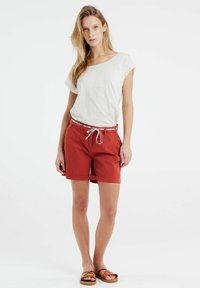 Rode katoenen shorts met een opgerolde zoom, voorzien van een gestreepte trekkoordriem. Gecombineerd met een losse witte t-shirt.