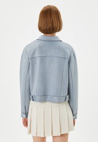 Lichtblauwe suède jas met een kraag, lange mouwen en een cropped ontwerp. Heeft gebuttonde manchetten en een vlakke achterkant.