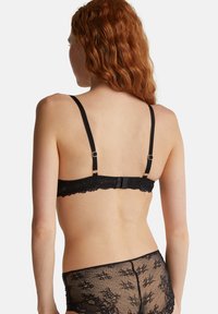 Černá krajková podprsenka s nastavovacími ramínky a zapínáním na háček, zdobená vlnkovaným okrajem a složitými květinovými vzory, spolu s odpovídajícími krajkovými šortkami.
