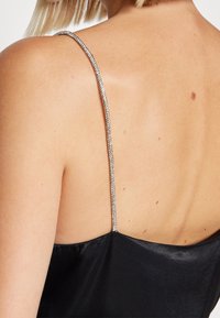 Robe en satin noir avec une fine bretelle argentée scintillante. Texture lisse, éclat subtil et design épuré mettant en valeur le dos.