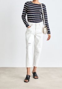 Haut à manches longues rayé bleu marine et rose, jean blanc taille haute avec déchirure, mules noires ouvertes, sac bandoulière crème, design minimaliste.