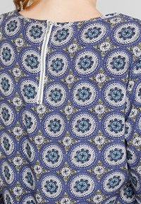 Tessuto blu con motivo a cerchi in diverse tonalità, con dettagli di chiusura con cerniera sul retro e una finitura liscia e testurizzata.