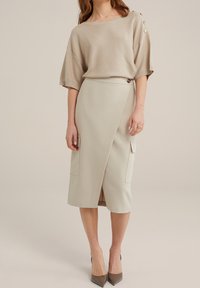 Beige stickad tröja med vida ärmar och knappaccenter, i kombination med en ljusbeige pennkjol med två framfickor och en sidoklyvning.