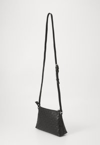 Borsa a tracolla nera con un motivo texturizzato e spallaccio regolabile esposta su uno sfondo bianco semplice.