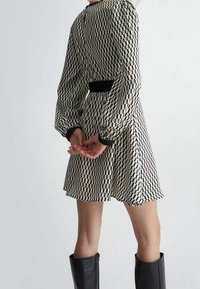 Robe à motifs noir et blanc avec des manches bouffantes, taille noire ajustée et jupe évasée, agrémentée de bottes noires montantes.