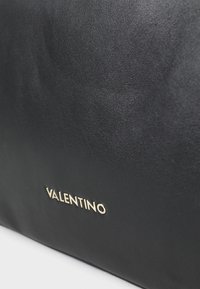 Fekete bőr táska sima felülettel és feltűnő arany "VALENTINO" logóval. A dizájn letisztult és minimalista.