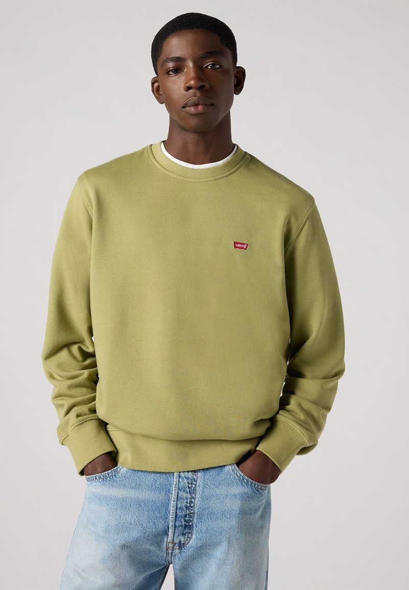 Sudadera verde oliva hecha de una tela suave, con un cuello redondo, mangas largas y un pequeño logo rojo de Levi's en el pecho. Los jeans son de un azul claro.