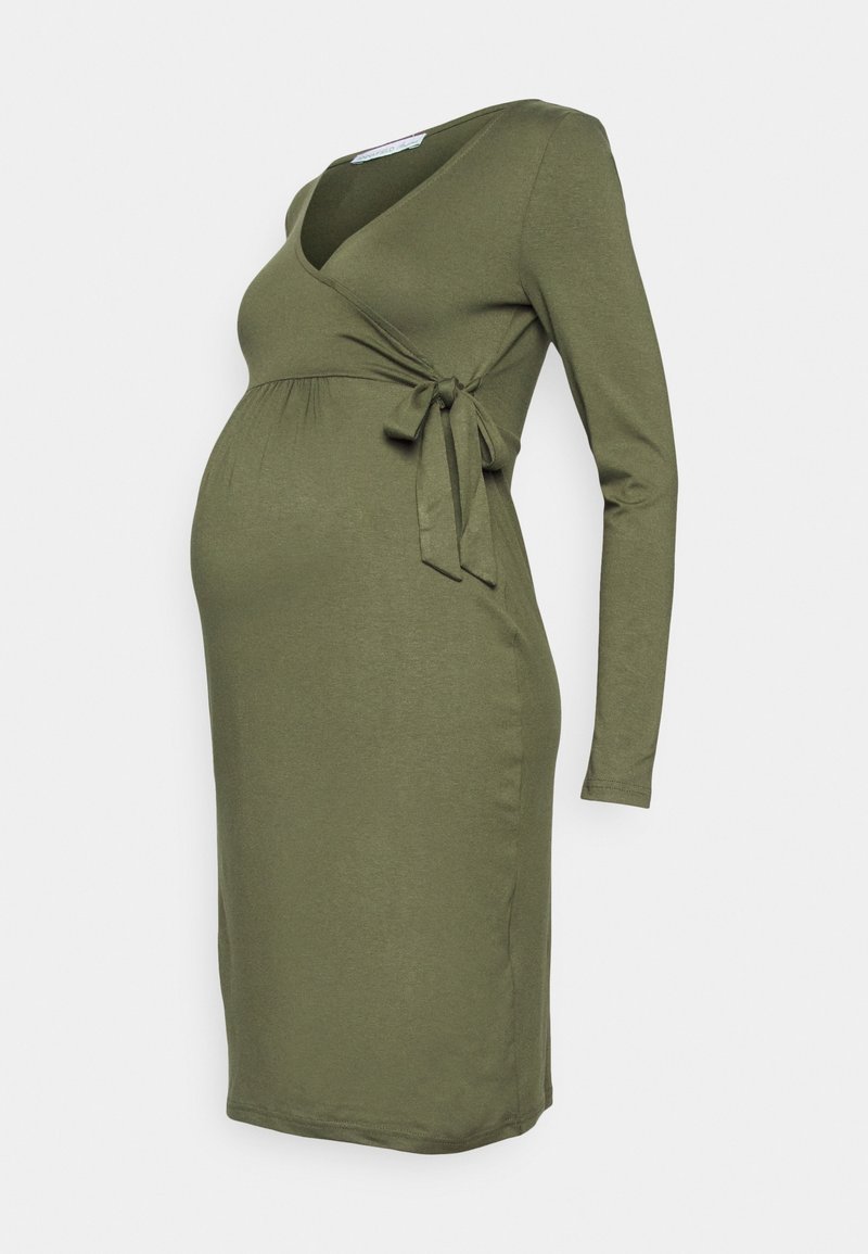 Robe de maternité vert olive à manches longues avec devant croisé et détail de nouage sur le côté, longueur genou, sur un fond clair uni.