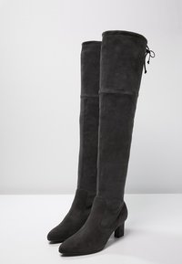 Bottes en daim gris montant jusqu'au genou, avec un bout pointu et un talon bloc. Caractérisées par une texture lisse et un détail à lacets à l'arrière.