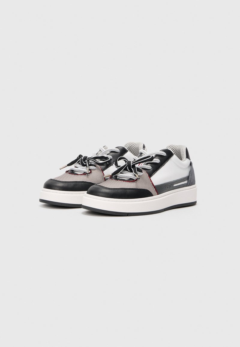 Baskets noires et blanches en matériaux mesh et cuir, avec des accents gris et des lacets plats, sur une semelle blanche à surface texturée.