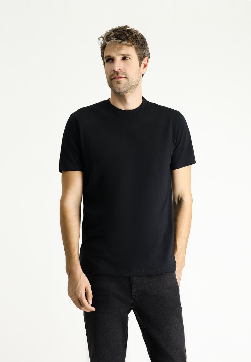 Camiseta negra de manga corta hecha de tejido suave con cuello redondo, combinada con jeans oscuros. Diseño simple, sin patrones ni acentos visibles.