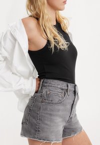 Gray denim shorts with a frayed hem, featuring copper-tone hardware and side pockets, paired with a black ribbed tank top and white oversized shirt.