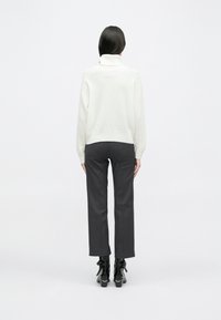 Λευκό πλεκτό πουλόβερ με ψηλό γιακά, ραβδωτές μανσέτες και στρίφωμα. Συνδυάζεται με εφαρμοστά σκούρα γκρίζα παντελόνια και μπότες αστραγάλου με χαρακτηριστικές λεπτομέρειες.