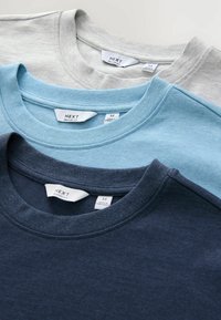 Három crewneck póló világosszürke, világoskék és sötétkék színben, puha pamutból készült, címkékkel a nyaknál, amelyek méretinformációt tartalmaznak.