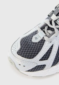 Baskets de sport grises avec une tige en mesh texturé et des accents synthétiques blancs. Design courbé avec un bout arrondi et des détails de laçage.