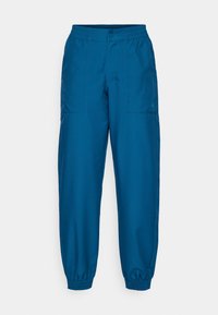 Modré joggers s elastickým pasem a volným střihem, které mají dvě boční kapsy a decentní logo na levé nohavici. Hladká, lehká tkanina.