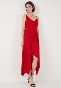 Rotes ärmelloses Kleid mit tiefem V-Ausschnitt, ausgestelltem Saum und asymmetrischem Schnitt. Hergestellt aus leichtem Stoff, hat es einen seitlichen Schlitz und eine glatte Textur.