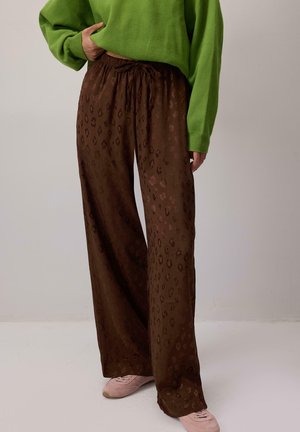 Pantalons marron à jambes larges avec un motif léopard subtil, dotés d'une taille élastique et d'une fermeture à cordon, associés à un pull vert.