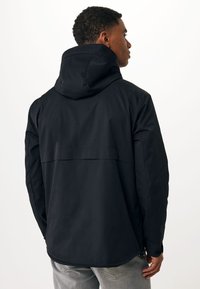 Sort vandtæt jakke med hætte, rygpaneldetalje og justerbare manchetter. Har en glat tekstur og minimalistisk design.