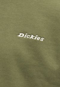 Tissu vert olive avec logo "Dickies" brodé en blanc au centre du matériau.