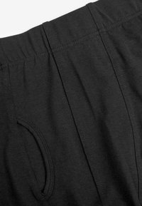 Pantaloni in cotone neri con cintura elastica, tasche laterali e cuciture pulite. Il tessuto presenta una consistenza morbida e una superficie liscia.