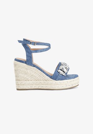 Blue denim wedge sandals with a textured jute heel, adjustable ankle strap, and decorative crystal embellishment on the toe.
