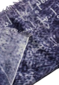 Tessuto viola con una consistenza morbida, caratterizzato da un motivo astratto sbiadito e bordi sfrangiati, che evidenzia una fusione di tonalità chiare e scure.