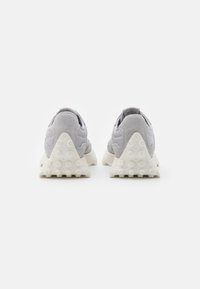 Zapatillas de ante gris y material sintético con una suela de goma texturizada blanca; presentan una forma triangular y una pestaña en la parte trasera para facilitar el uso.