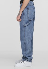 Light blue denim cargo pants with a relaxed fit, featuring back pockets and a side belt loop. Paired with white sneakers.