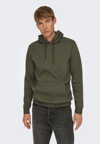 Sudadera de color verde oscuro hecha de tela suave, con un bolsillo frontal y capucha con cordón. Presenta puños y dobladillo acanalados para un ajuste ceñido.