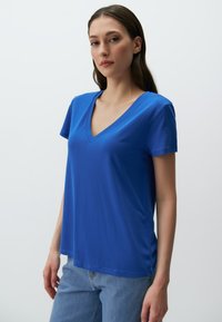 Królowsko-niebieska koszulka z dekoltem w serek, wykonana z gładkiego, lekkiego materiału. Krótkie rękawy, luźny krój i prosty dół.
