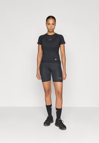 Čierny športový outfit pozostávajúci z krátkeho rukávu a obtiahnutých šortiek, obidva s jemným logom. Materiál sa zdá byť hladký a elastický.