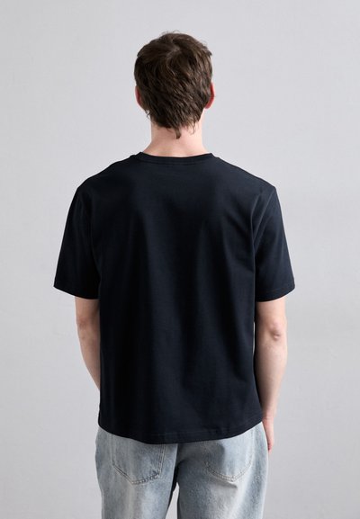 Camiseta de algodón negra de mangas cortas y cuello redondo, vista desde atrás, combinada con jeans de mezclilla azul claro.