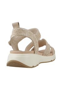Sandalias beige con correas de tela trenzada, correa ajustable en el tobillo, plantilla acolchada y suela de goma blanca. Diseño plano con acentos texturizados.