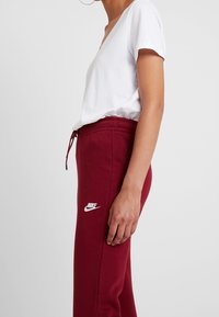 Vinnande bourgognefärgade sweatpants med elastiskt midjeband och dragsko; har den vita Nike-logotypen p å låret. Tillsammans med en enkel vit T-shirt med V-ringning.